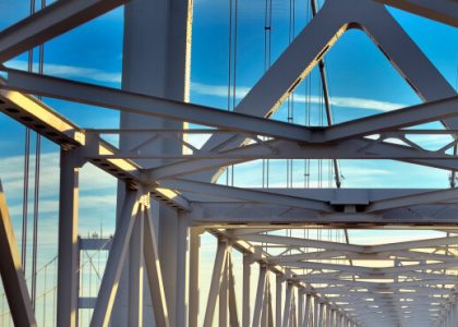 A bridge’s beams and supporting structure against a blue sky.