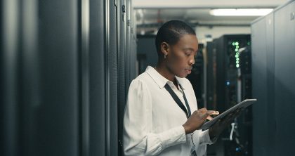 A man stands in front of servers in a server while holding a diagnostic tool.