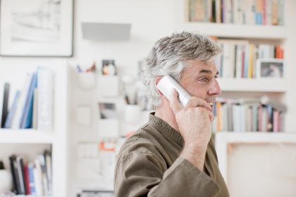 A bearded, middle aged man is speaking on a cordless telephone.
