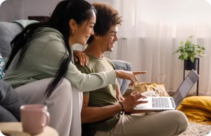 A couple sitting on a couch and working on a laptop together.