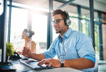 A customer service representative is on the phone via headset and is using a computer in an office.