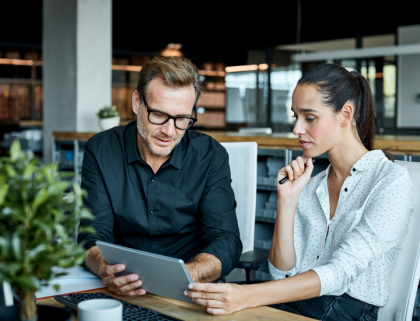 A man and woman look at a tablet and have a discussion in a business setting.