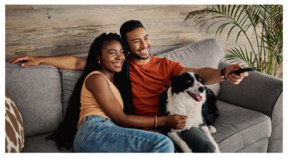 Couple and dog sitting on the couch smiling while holding TV remote