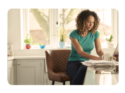 Woman sitting on chair in kitchen with laptop and coffee mug