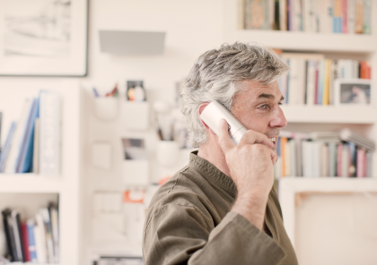 Man holding a white home phone up to his ear