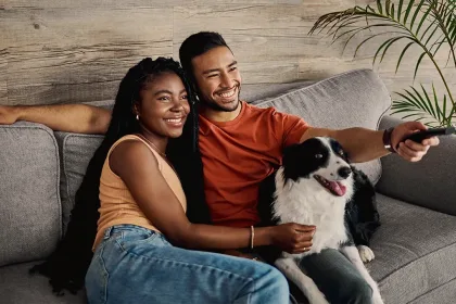A couple watching TV on a couch with their dog.