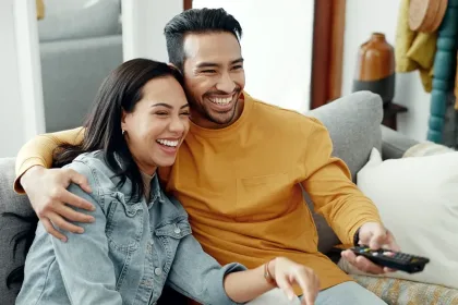 A couple smiling and watching TV together in their living room.