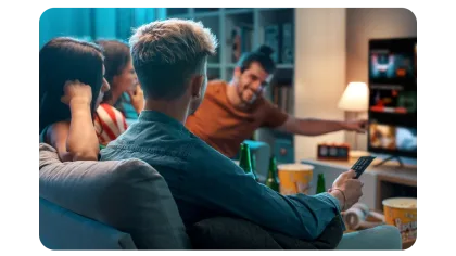 Group of friends sitting on a couch, watching TV together, with snacks and drinks on the table in a cozy living room.