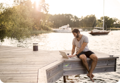 Man sitting on dock while looking at a laptop