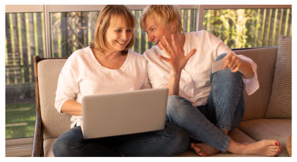 Two women sitting on a couch looking at a laptop